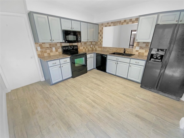 kitchen featuring decorative backsplash, light wood-style floors, light stone countertops, black appliances, and a sink