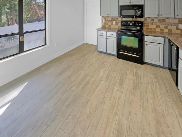 kitchen featuring black appliances, light wood-style flooring, light stone counters, and backsplash