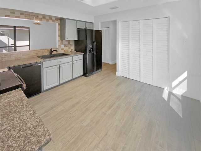 kitchen featuring a sink, light countertops, light wood-type flooring, black appliances, and tasteful backsplash