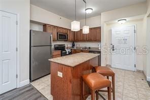 kitchen featuring electric stove, a kitchen island, stainless steel microwave, freestanding refrigerator, and hanging light fixtures