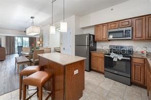 kitchen with stainless steel appliances, brown cabinets, a kitchen island, and hanging light fixtures