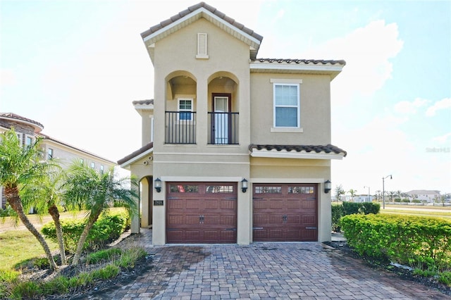 mediterranean / spanish-style home featuring a garage, decorative driveway, a tile roof, and stucco siding