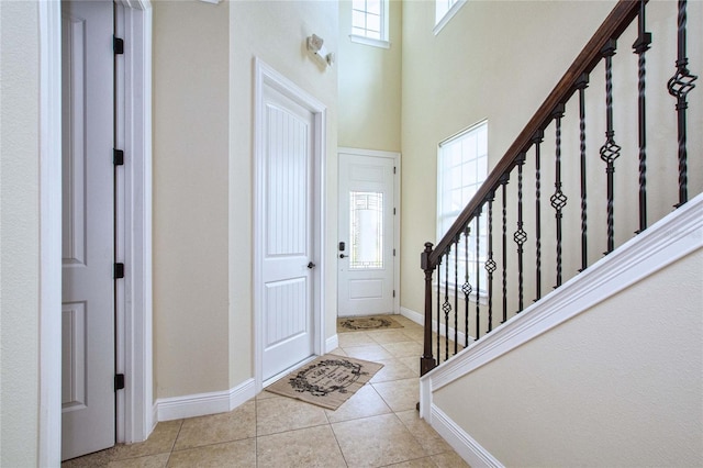 entryway with light tile patterned floors, a high ceiling, stairs, and baseboards