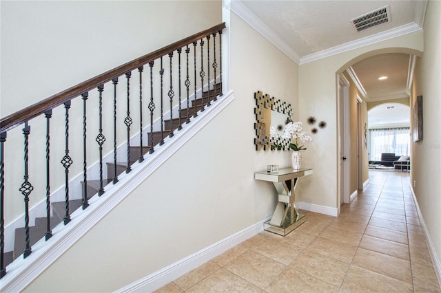 staircase featuring arched walkways, crown molding, visible vents, tile patterned flooring, and baseboards