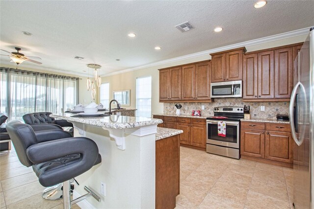 kitchen featuring visible vents, open floor plan, appliances with stainless steel finishes, backsplash, and brown cabinets