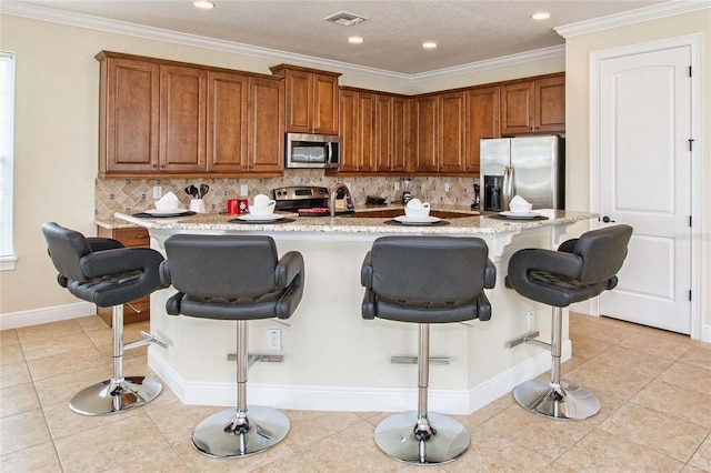 kitchen with brown cabinetry, visible vents, stainless steel appliances, and light tile patterned flooring