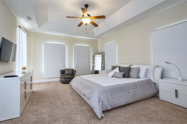 carpeted bedroom with a tray ceiling, a ceiling fan, visible vents, and baseboards