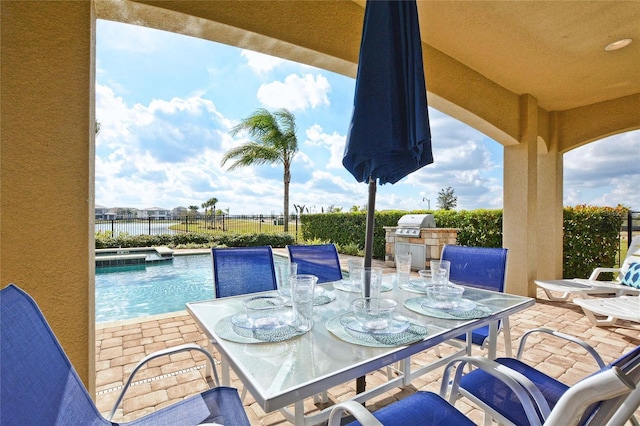 view of patio / terrace featuring outdoor dining area, a pool with connected hot tub, area for grilling, fence, and exterior kitchen