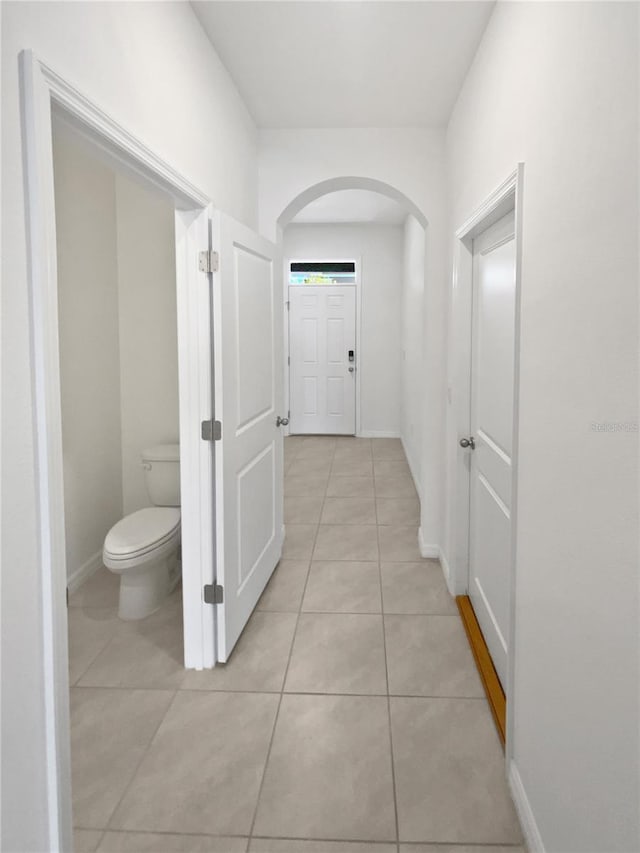 corridor with arched walkways, light tile patterned floors, and baseboards