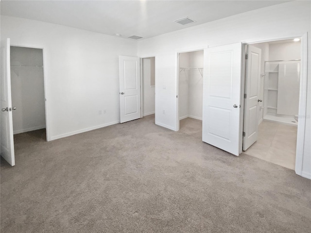 unfurnished bedroom featuring visible vents, baseboards, a closet, carpet, and a walk in closet