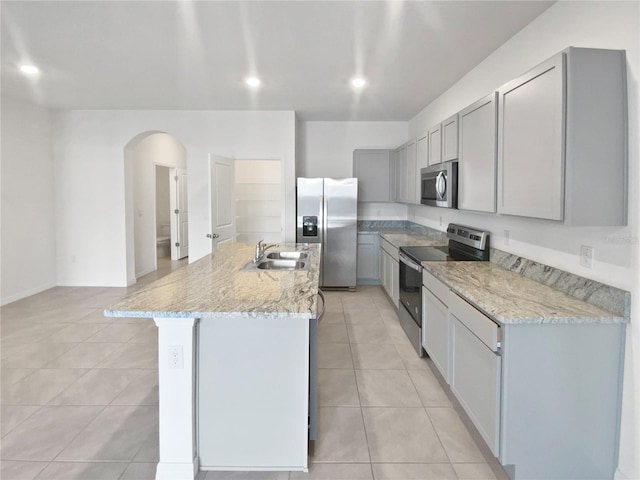 kitchen featuring light tile patterned floors, arched walkways, gray cabinetry, stainless steel appliances, and a sink