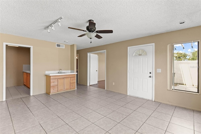 unfurnished living room featuring light tile patterned floors, visible vents, ceiling fan, a textured ceiling, and a sink