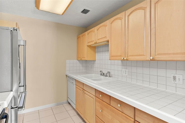 kitchen featuring visible vents, freestanding refrigerator, white dishwasher, light brown cabinets, and a sink