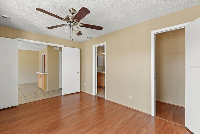 unfurnished bedroom with light wood-type flooring, ensuite bath, a ceiling fan, and a textured ceiling