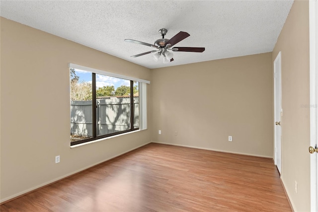 spare room with a textured ceiling, light wood finished floors, a ceiling fan, and baseboards