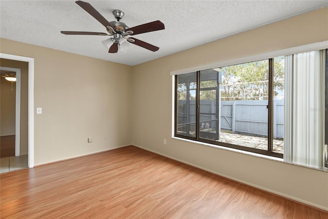 spare room with light wood-style floors, ceiling fan, a textured ceiling, and baseboards