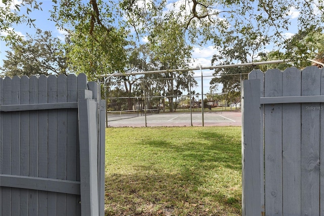 view of yard with a tennis court, a gate, and fence