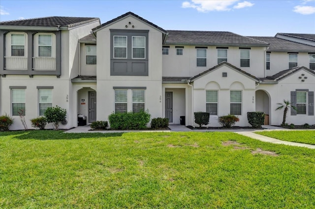 townhome / multi-family property featuring a front lawn, a tiled roof, and stucco siding