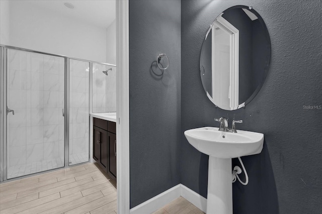 full bath with wood finish floors, a stall shower, a sink, baseboards, and a textured wall