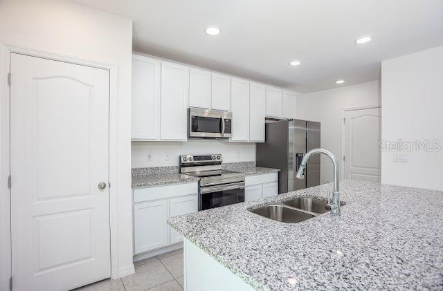 kitchen featuring light stone counters, stainless steel appliances, white cabinets, a sink, and light tile patterned flooring