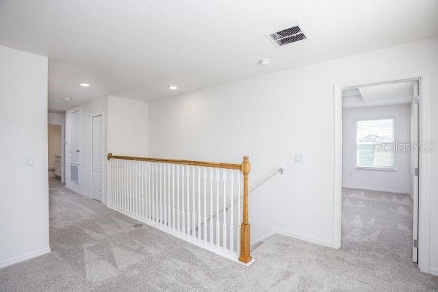 hallway featuring carpet floors, baseboards, visible vents, and an upstairs landing