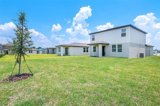 rear view of property featuring central AC unit and a lawn