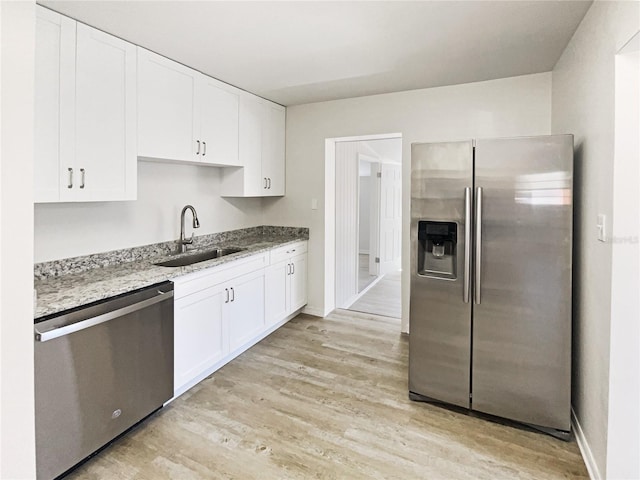 kitchen featuring appliances with stainless steel finishes, a sink, light stone counters, and white cabinets