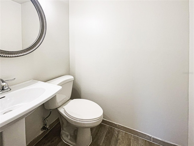 half bath featuring baseboards, toilet, and wood finished floors