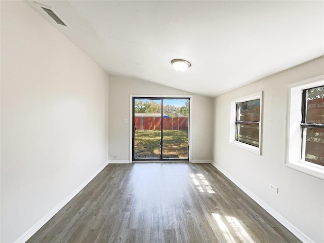 empty room with dark wood-style floors, visible vents, vaulted ceiling, and baseboards