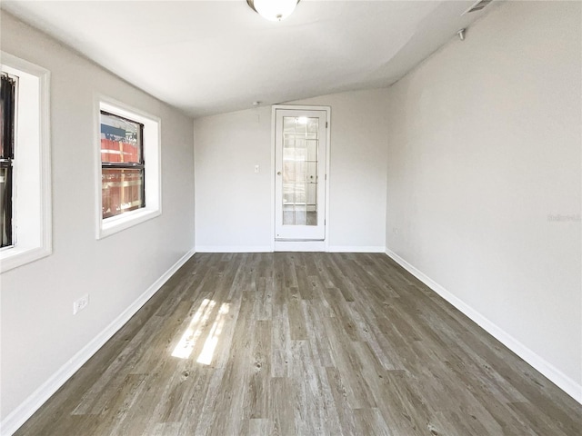 empty room featuring vaulted ceiling, baseboards, and wood finished floors