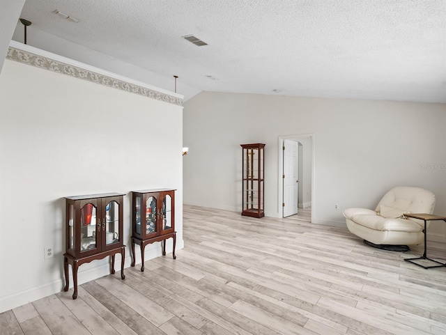 sitting room featuring light wood finished floors, baseboards, visible vents, lofted ceiling, and a textured ceiling