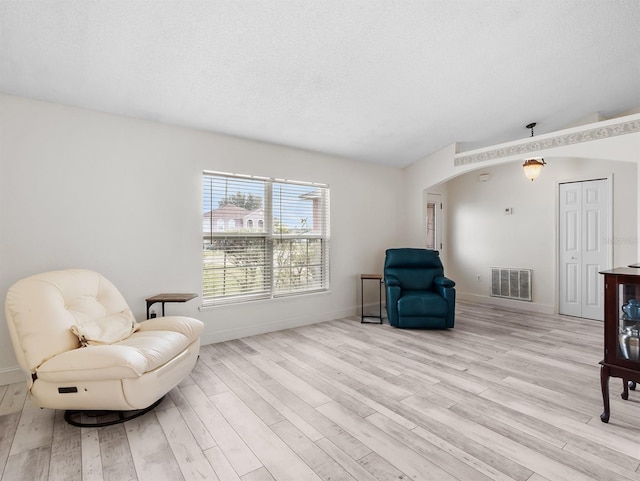 living area with arched walkways, a textured ceiling, wood finished floors, and visible vents