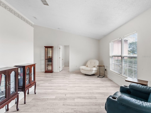 sitting room featuring vaulted ceiling, a textured ceiling, visible vents, and light wood-style floors