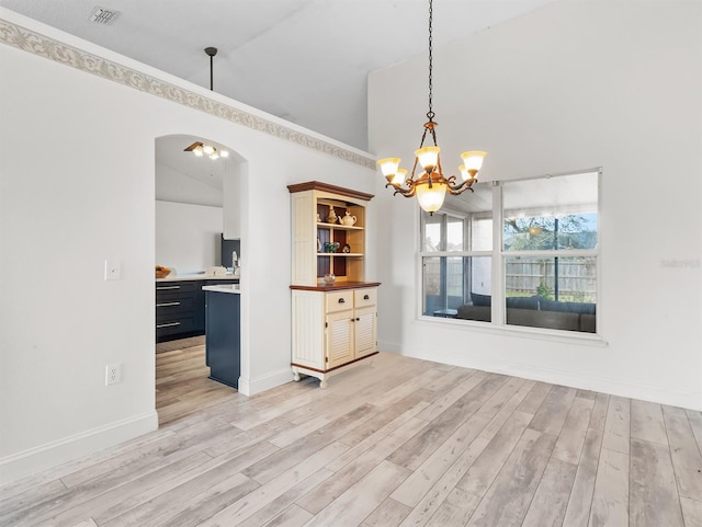 unfurnished dining area featuring arched walkways, light wood-style flooring, visible vents, and an inviting chandelier