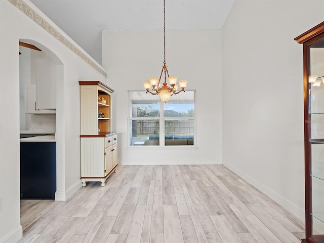 unfurnished dining area featuring arched walkways, baseboards, a notable chandelier, and light wood-style floors