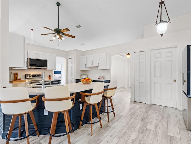 kitchen with arched walkways, a breakfast bar area, stainless steel appliances, a peninsula, and light wood-style floors