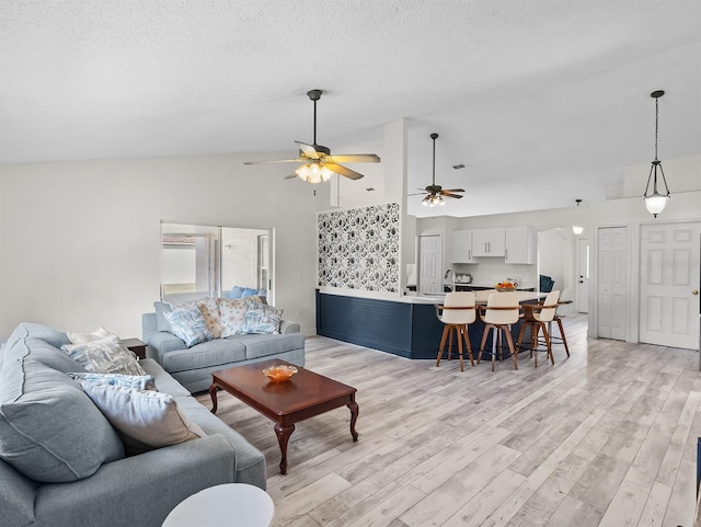 living area with a textured ceiling, high vaulted ceiling, light wood finished floors, and a ceiling fan