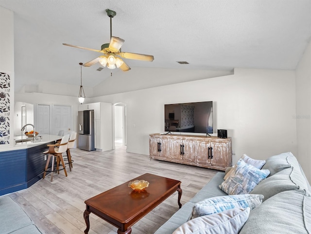 living area featuring arched walkways, ceiling fan, light wood finished floors, and visible vents