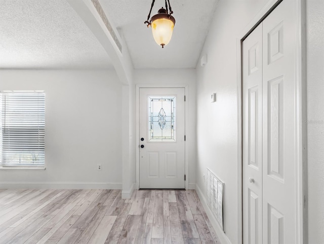 doorway featuring light wood finished floors, baseboards, visible vents, arched walkways, and a textured ceiling