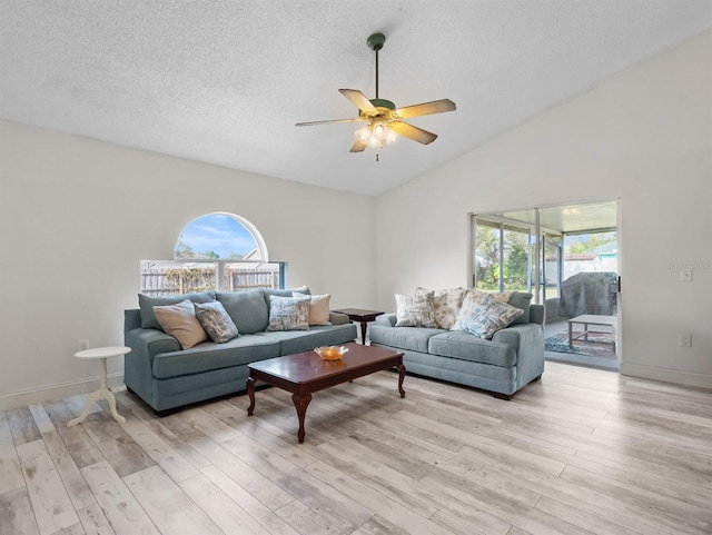 living area featuring light wood-style flooring, vaulted ceiling, a textured ceiling, ceiling fan, and baseboards