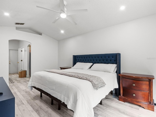 bedroom featuring arched walkways, a textured ceiling, lofted ceiling, visible vents, and light wood-style floors