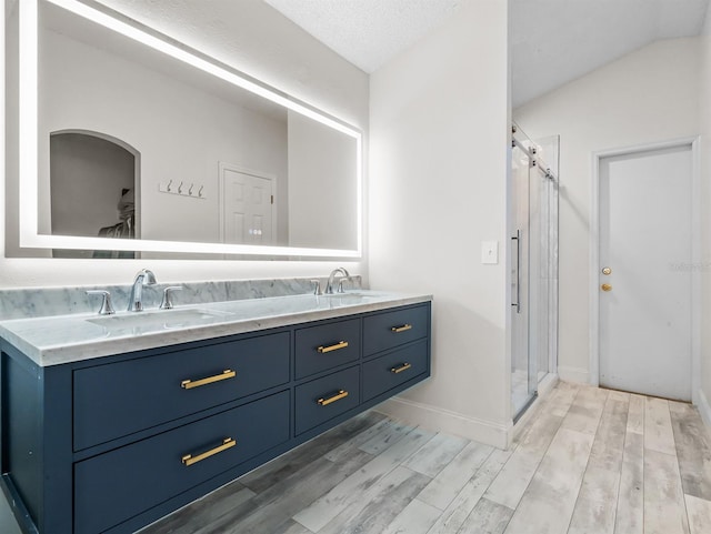 bathroom featuring double vanity, a shower stall, a sink, and wood finished floors