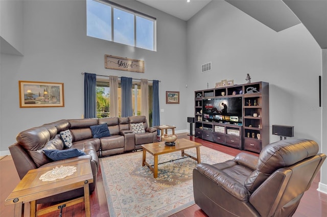 living room featuring baseboards, a high ceiling, visible vents, and wood finished floors