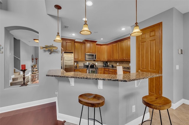 kitchen with stainless steel appliances, dark stone countertops, a breakfast bar area, and tasteful backsplash