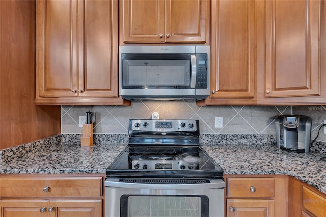 kitchen with stainless steel appliances, dark stone countertops, brown cabinets, and decorative backsplash