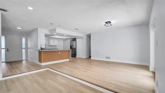 kitchen featuring light wood finished floors, visible vents, open floor plan, a textured ceiling, and stainless steel refrigerator with ice dispenser