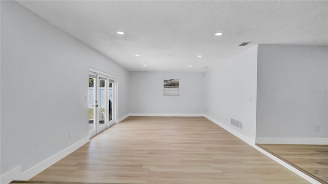 empty room featuring light wood finished floors, visible vents, and a textured ceiling