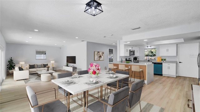 dining space featuring a healthy amount of sunlight, light wood-style flooring, visible vents, and a textured ceiling