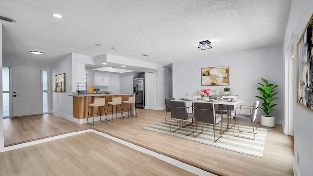 dining room with recessed lighting, visible vents, light wood-style flooring, a textured ceiling, and baseboards