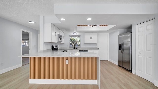 kitchen featuring stainless steel appliances, a peninsula, a sink, light wood-style floors, and light countertops